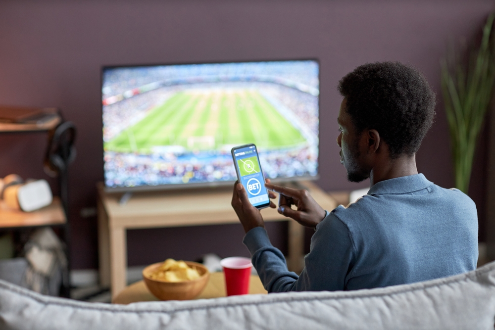 Back,View,Of,Man,Holding,Smartphone,With,Sports,Bets,App 